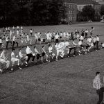 Dressed in their street clothes, band members practice in a field on campus.