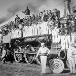 Members of the 1925 Million Dollar Band standing on and in front of a steam train.