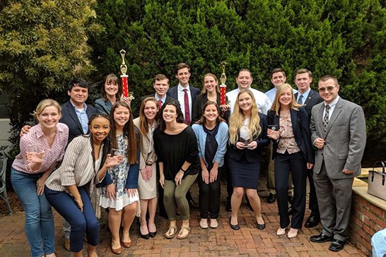 A group of students on the mock trial team hold two trophies