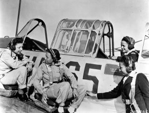 A black and white photo of the Tuskegee Airwomen with a plane.