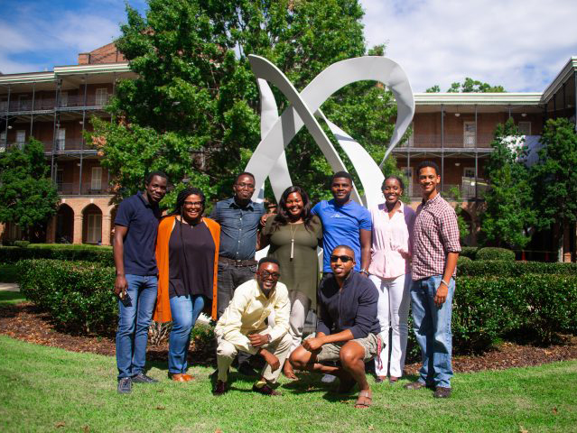 new math department graduate students standing in front of a sculpture in Woods Quad