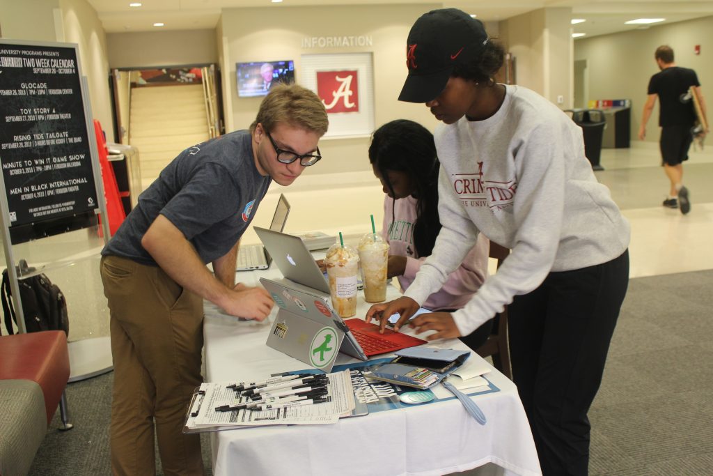 A student helps another student register to vote at a table.