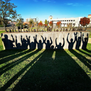 Shadows of students with their hands up in front of a statue of children with their hands up.