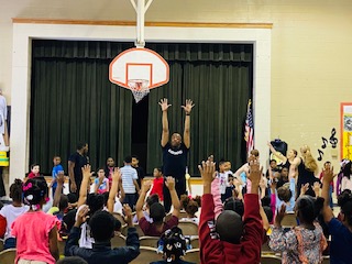 A dancer leads elementary students in a stretch.
