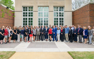 students in the Randall Research Scholars Program stand in a line outside the Paul W. Bryant Museum with UA president Dr. Stuart Bell