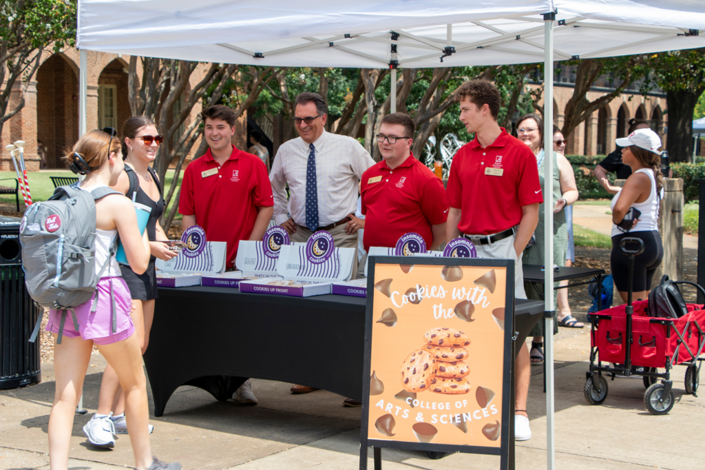 Dr. Joseph Messina and three Arts and Sciences Ambassadors handing out cookies to students 